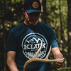 Inspecting a deer antler in the woods wearing the midnight navy t-shirt